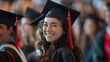 cute brunette graduate girl in black mortarboard and gown smiles happily, holding diploma amidst blurred classmates in celebration