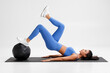 © nikolas_jkd - Fitness woman doing glute bridge exercise with med ball on gray background. Athletic girl working out