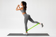 © nikolas_jkd - Athletic girl doing exercise for glutes with resistance band on gray background. Fitness woman working out.