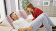 © Krakenimages.com - A woman in red leaning over a laughing man in a white shirt on a bed, portraying love in a cozy bedroom setting.