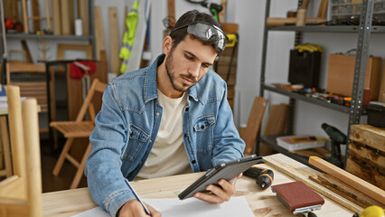 Wall Mural - Handsome hispanic man planning woodworking projects in a carpentry studio