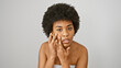 A thoughtful african american woman with curly hair poses against a white background, touching her face gently.