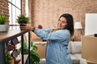 © Krakenimages.com - Young beautiful plus size woman smiling confident putting plant on shelving at new home