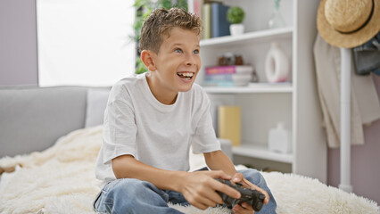 Wall Mural - Adorable blond boy, happily engrossed in gaming, comfortably sitting on sofa at home, confidently using gaming device, radiating pure joy.