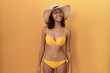 Young hispanic woman wearing bikini and summer hat looking away to side with smile on face, natural expression. laughing confident.