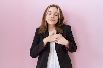 Wall Mural - Young caucasian business woman wearing black jacket smiling with hands on chest with closed eyes and grateful gesture on face. health concept.