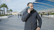 © Krakenimages.com - Handsome hispanic man talking on a smartphone outdoors in a sunny city with palm trees and modern architecture.