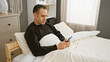 © Krakenimages.com - Handsome hispanic man relaxing in bedroom using smartphone, conveying modern indoor lifestyle