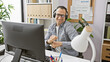 © Krakenimages.com - A smiling hispanic man wearing headphones dances while seated at his office desk, exuding joy and positivity in a modern workplace.