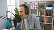 © Krakenimages.com - Handsome hispanic man speaking into microphone in a radio studio setting, wearing headphones.