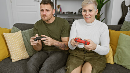 Wall Mural - A woman and a man are playing video games together on a couch in a cozy living room interior.