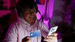 © Krakenimages.com - Attractive young hispanic man streamer, all smiles while streaming game night in the dark gaming room. smartphone, credit card at hand, he's living the virtual gamer life.
