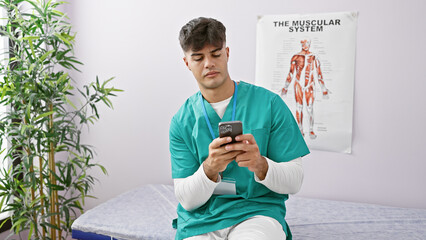 Sticker - Young, handsome hispanic man physiotherapist sporting a serious face while using a smartphone in a bustling rehab clinic