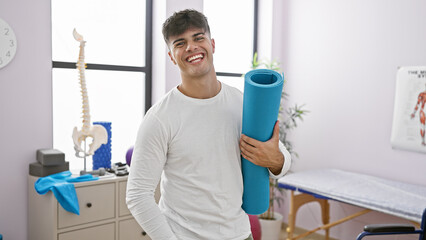 Sticker - Young, smiling hispanic guy packing fitness with confidence, sporty man with yoga mat at rehab clinic, embracing athletic lifestyle for a fitter him