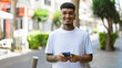© Krakenimages.com - Smiling young latin man happily texting on his smartphone outdoors, a handsome tattooed adult immersed in a cheerful digital conversation on the urban street.