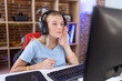 Young caucasian woman playing video games wearing headphones hand on mouth telling secret rumor, whispering malicious talk conversation