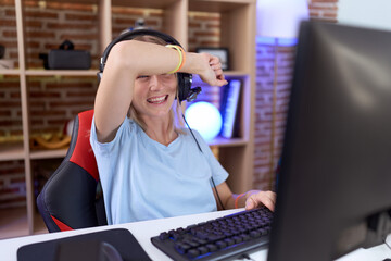 Poster - Young caucasian woman playing video games wearing headphones covering eyes with arm smiling cheerful and funny. blind concept.