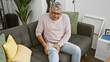 Middle-aged man with grey hair experiencing leg pain while sitting on a couch in a cozy living room interior.