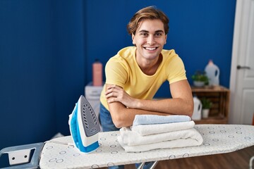 Wall Mural - Young caucasian man smiling confident leaning on ironing board at laundry room