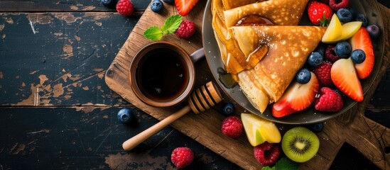 Wall Mural - A plate filled with fruit-topped pancakes sits next to a steaming cup of coffee on a wooden table. The pancakes are garnished with honey and a variety of fresh fruits.