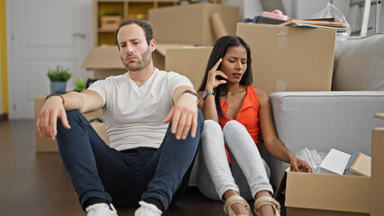 Wall Mural - Beautiful couple sitting on floor together witt worried expression at new home