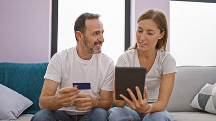 Sticker - Father and daughter using touchpad and credit card sitting on sofa smiling at home