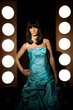 Plastic mannequin with a blue princess ball gown posing between rows of spotlights. Dummy with a blue satin dress and a black wig posing in a fashion mode.