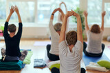 Fototapeta Sport - A group of senior women engage in various yoga exercises, including neck, back, and leg stretches, under the guidance of a trainer in a sunlit space, promoting well-being and harmony