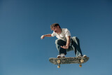 Active man doing tricks in the air on his skateboard at the skate park on blue sky background