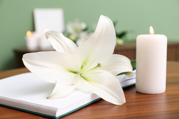 Wall Mural - Beautiful lily flower, burning candle and book on wooden table in room, closeup