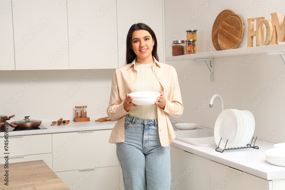 Beautiful young happy woman with clean dishes in kitchen