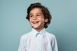 Cheerful little boy in white shirt looking at camera and smiling against blue background