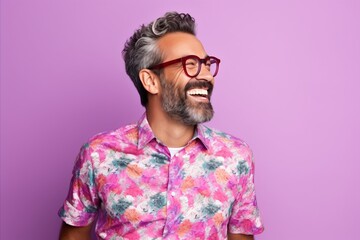 Wall Mural - Portrait of a handsome Indian man with gray hair and beard wearing colorful shirt and red glasses, standing against purple background