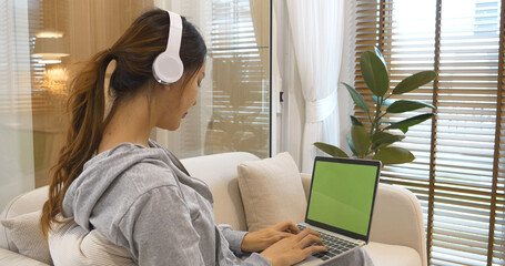 Happy asian woman use headphones listen to music online web conference sitting on cozy sofa in living room at home. Female asian people working at home research watching online e-learning video call