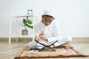 Wall Mural - Asian muslim boy reading Quran on prayer mat at home