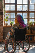 © ebhanu - A person with colored hair, wearing leg braces, sitting in a wheelchair in a loft.