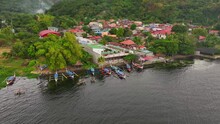 Aerial Orbit Shot Of Asian Neighborhood With Traditional Boats At Shore In Tropical Area Of Philippines. Taal Lake Scenery With Rising Smoke Of Fire.