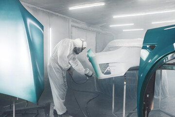 Wall Mural - Automobile repairman painter in protective workwear and respirator painting part of car in paint chamber.