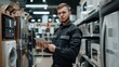 © buraratn - A young successful sales assistant in uniform with a tablet in his hands against the background of the interior of the hall in a home appliances and electronics store.