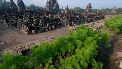 Wall Mural - Revealing tilting up shot of Candi Sewu or Thousand Temple from showing green plant view with ancient temple and blue sky background