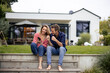 © Westend61 - Happy couple sitting on steps with smart phone in front of house