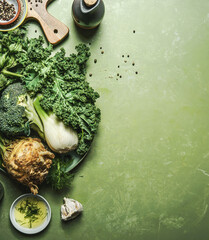 Food background with green vegetables ingredients on kitchen table with cutting board and cooking oil, top view. Healthy, clean and detox food