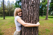 © Westend61 - Smiling young woman hugging tree trunk in forest