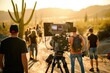 A film crew captures a scene during golden hour with a professional camera, amidst a desert scenery backlit by the setting sun.