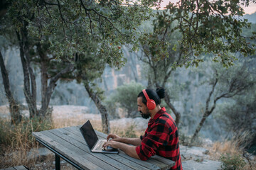 Wall Mural - A young man is working on a laptop at a camping site in the mountains.