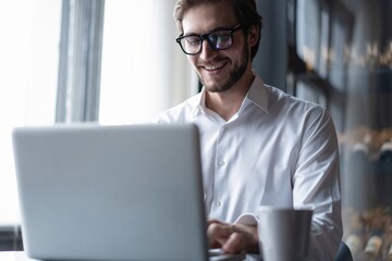 Wall Mural - Business portrait - businessman sitting in in office working with laptop computer. Middle age man in 30s with happy confident smile