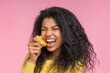 Portrait of beautiful young african american woman posing over pastel pink background pretending to bite a lemon cut in a half