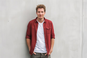 Wall Mural - Casual and Approachable Young Man in Red Button-Up Shirt Leaning Against White Wall