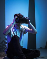 Young man wearing VR glasses sitting in a yoga pose on the virtual reality escape room floor. Fun, entertainment, and innovation concepts.