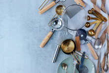 Various Kitchen Utensils On A Striped Kitchen Towel On A Gray Concrete Background. Sieve, Measuring Spoons, Knives, Pizza Cutter. Space For Text